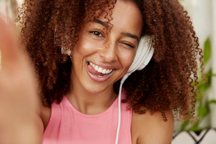 files/positive-woman-with-frizzy-bushy-hairdo-shows-tongue-makes-selfie-connected-unrecognizable-device-listens-favourite-songs-playlist-with-headphones-enjoys-free-time-alone-ethnicity-lif.avif